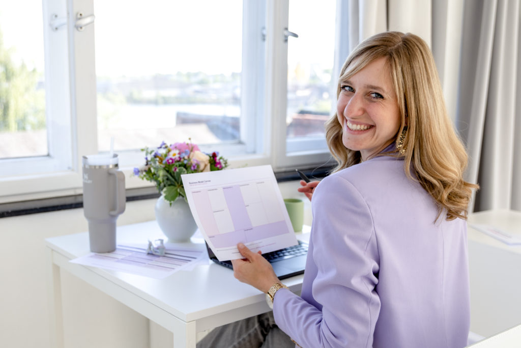 Madleen Frommholz sitzt lächelnd am Schreibtisch im hellen Büro mit Blick auf den Hafen und hält einen Businessplan zur Beantragung von Fördermitteln in der Hand