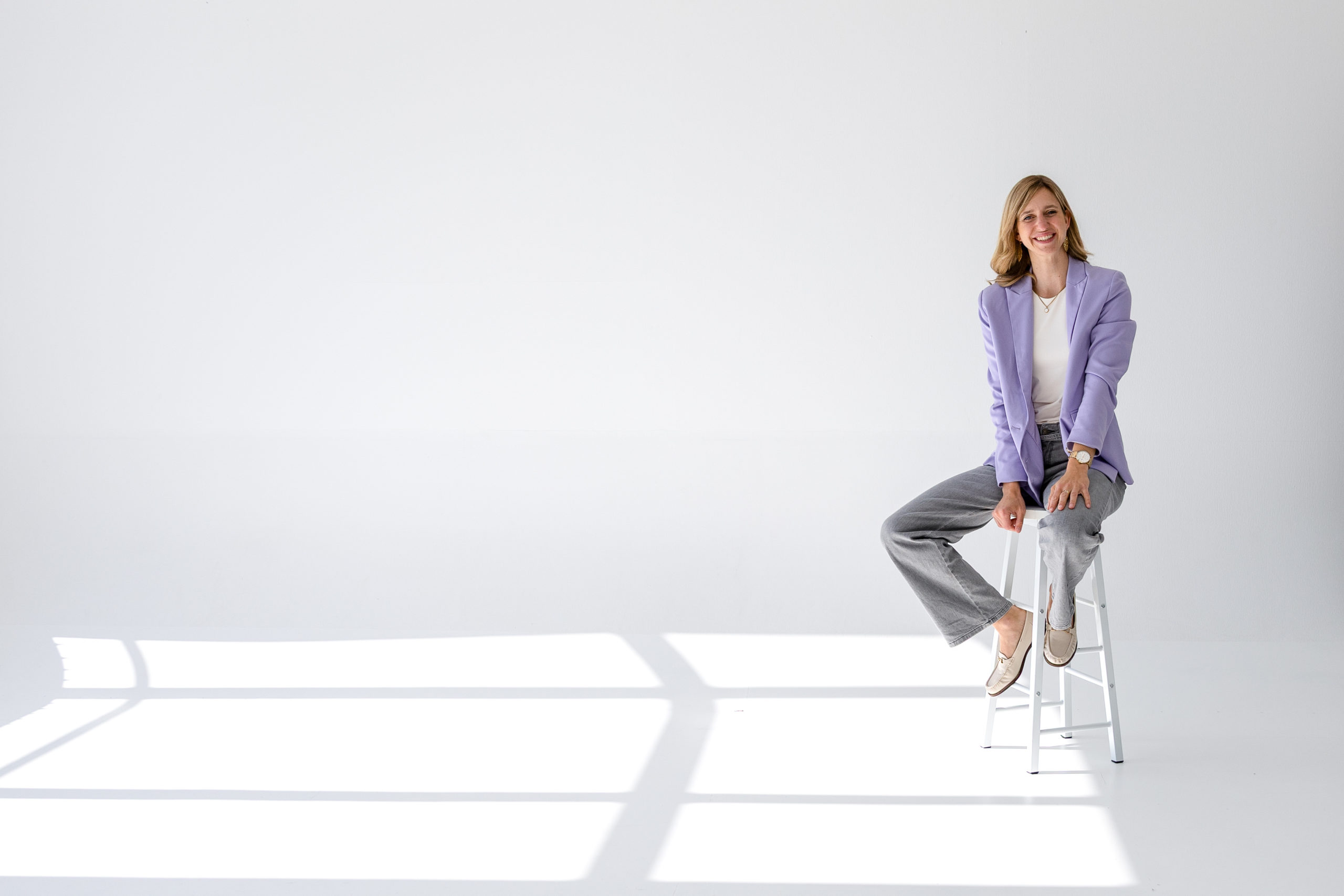 Madleen Frommholz sitzt im Business-Outfit auf einem Barhocker im modernen Büro beim Start in die Selbstständigkeit als Mutter