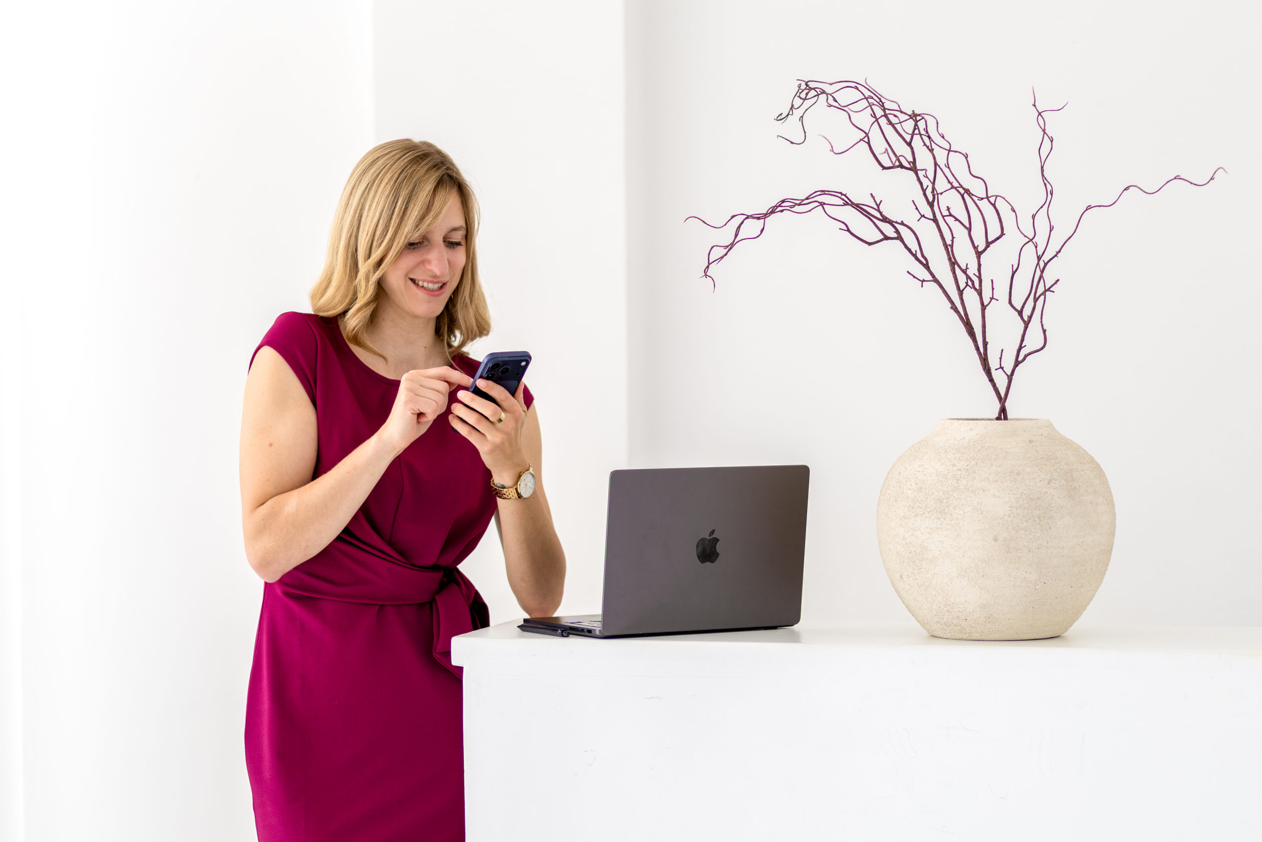 Madleen Frommholz steht mit Smartphone an einem Bürotresen neben einem Laptop und begleitet den erfolgreichen Weg vom Nebenberuf in die Selbstständigkeit.